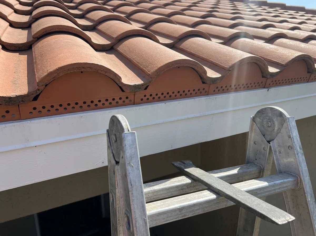 Eave of a barrel tile roof with a terracotta-colored metal bird stop closing the curved gaps under the first row of tiles