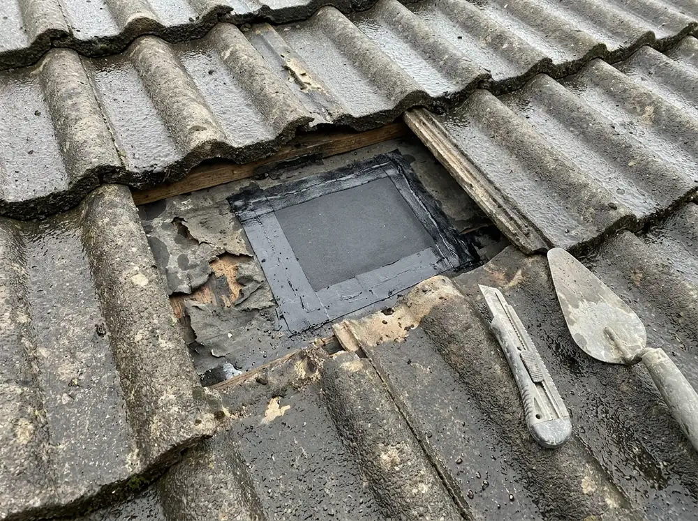 Small patch of new black underlayment sealed over a torn spot where several concrete roof tiles are missing