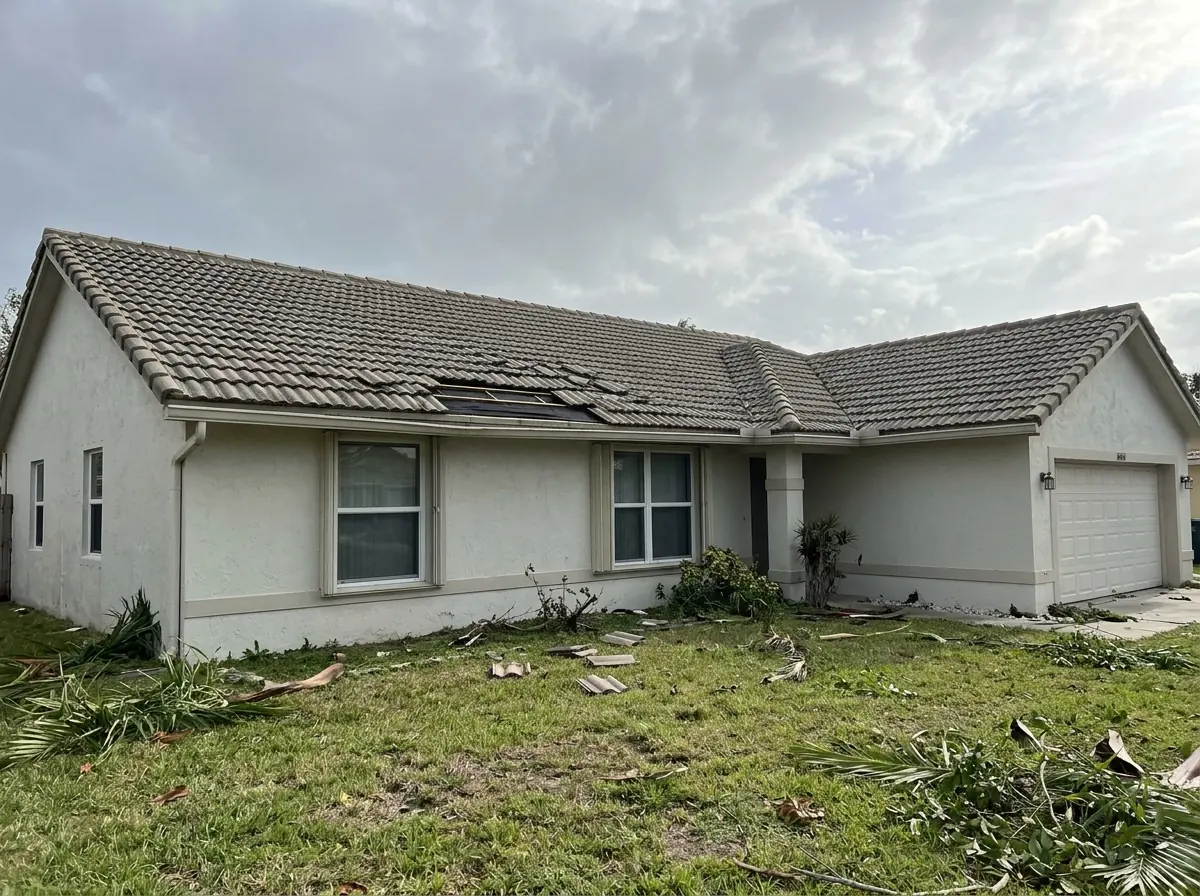 Concrete S-tiles shifted out of their rows and several missing near the eave of a single-story stucco house after a windstorm