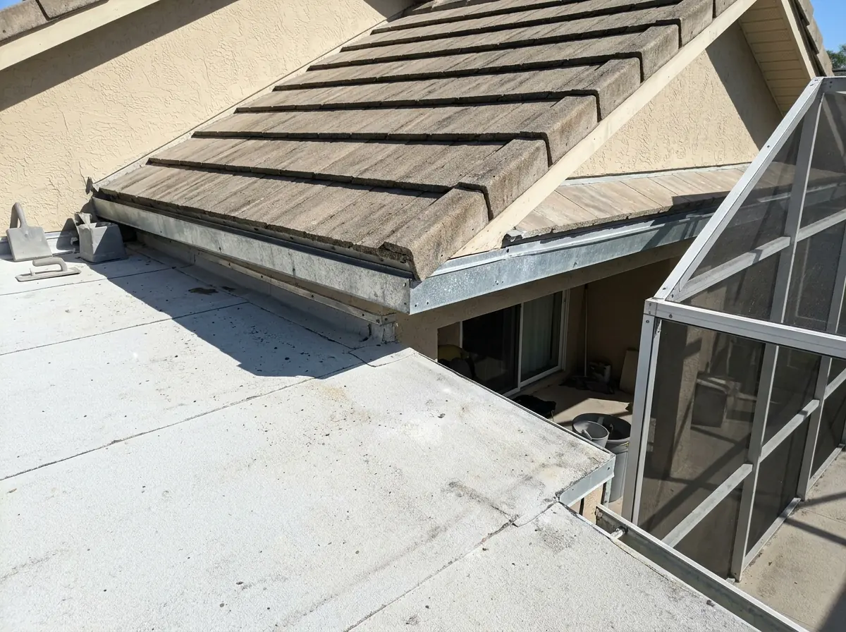 Edge where a concrete tile slope drains onto a low flat roof over a back porch, metal flashing along the joint