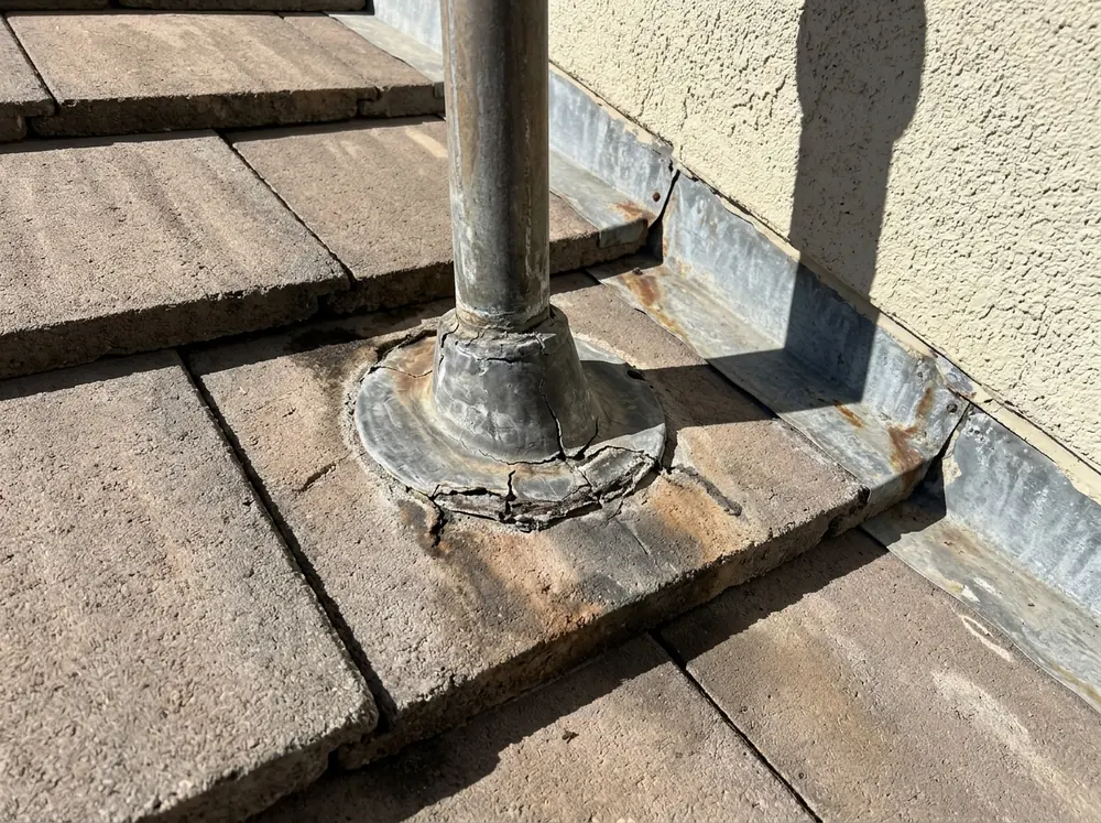 Lead pipe boot and step flashing where a tile roof meets a stucco wall, a crack visible in the boot flange